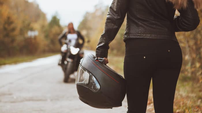 Motarde tenant un casque de moto à la main, moto sur une route de campagne 