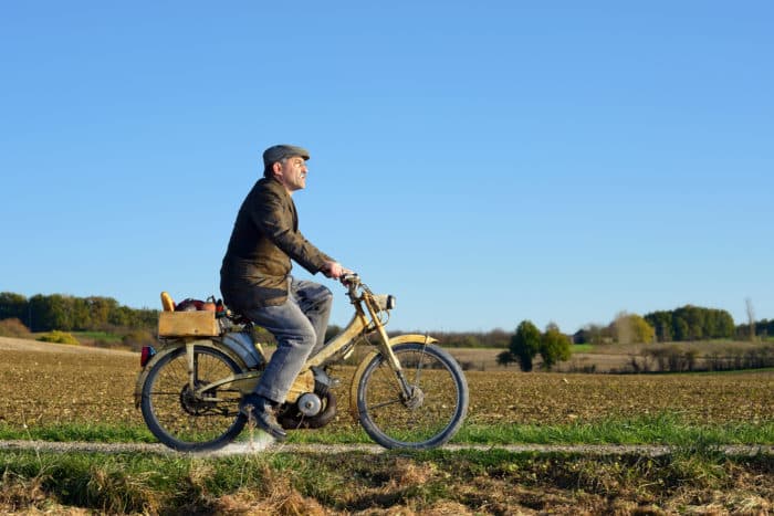 homme âgé qui fait de la mobylette sur une route de campagne 